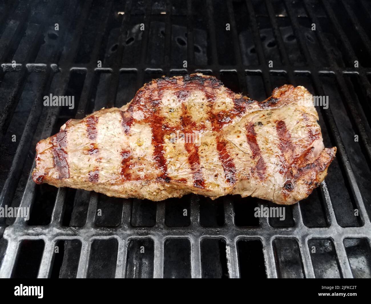 cooked steak meat on barbecue grill rack with liquid or marinade Stock