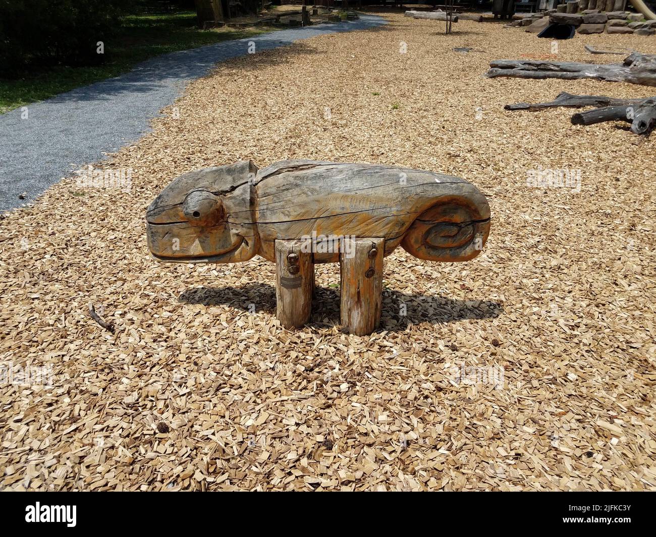 carved wooden lizard animal bench on playground with wood chips Stock