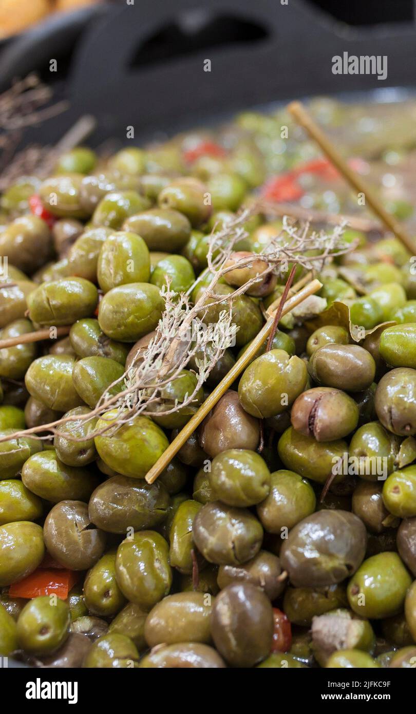 Green crushed marinated olives. Delicious pickled snack displayed plastic basket. Stock Photo