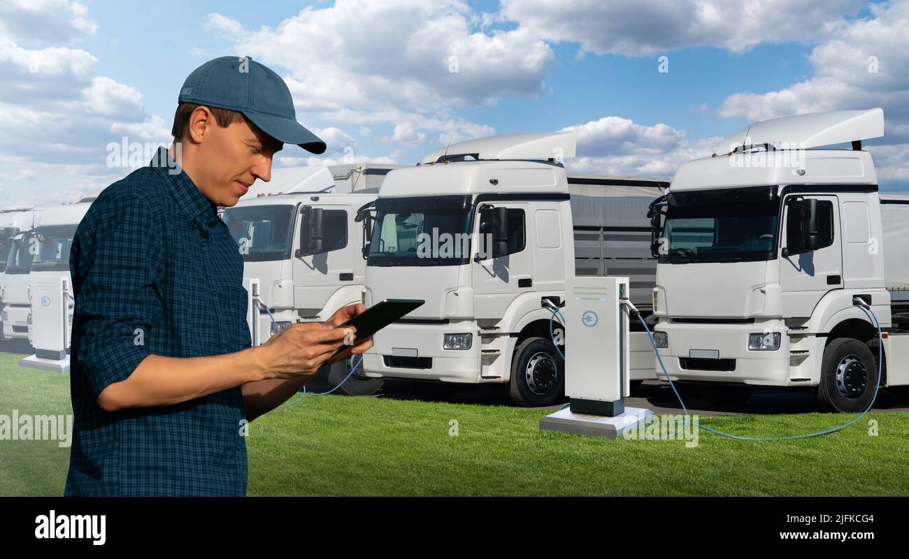 Fleet manager with a digital tablet stands next to electric trucks at electric vehicle charging