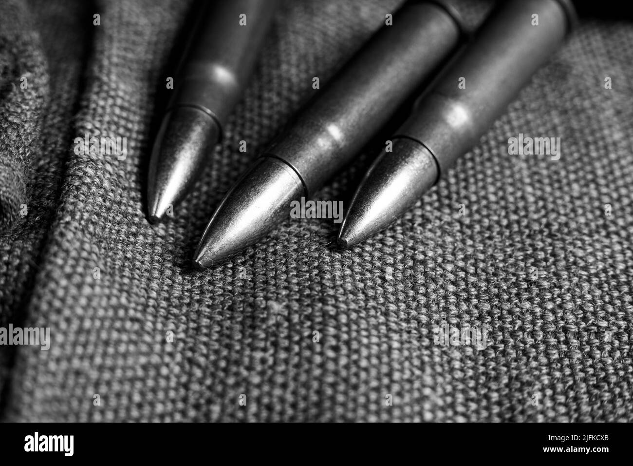 Three Ak-47 cartridges lying on a piece of military canvas, monochrome photo Stock Photo