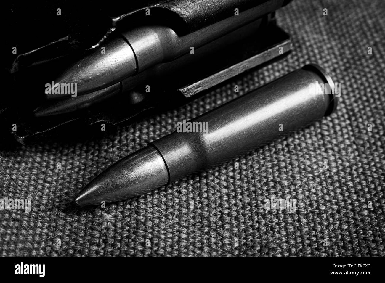 loaded magazine of Ak-47 and a single cartridge (7,62x39mm) lying on a military canvas background, monochrome photo Stock Photo