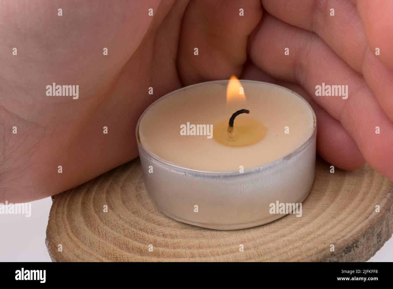 Hand protecting the burning candle placed on piece of wood Stock Photo