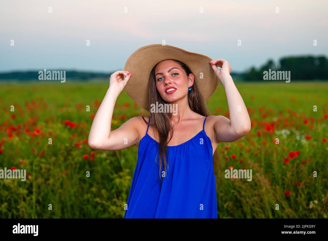 portrait of elegant young woman with long hair and straw hat in poppy ...