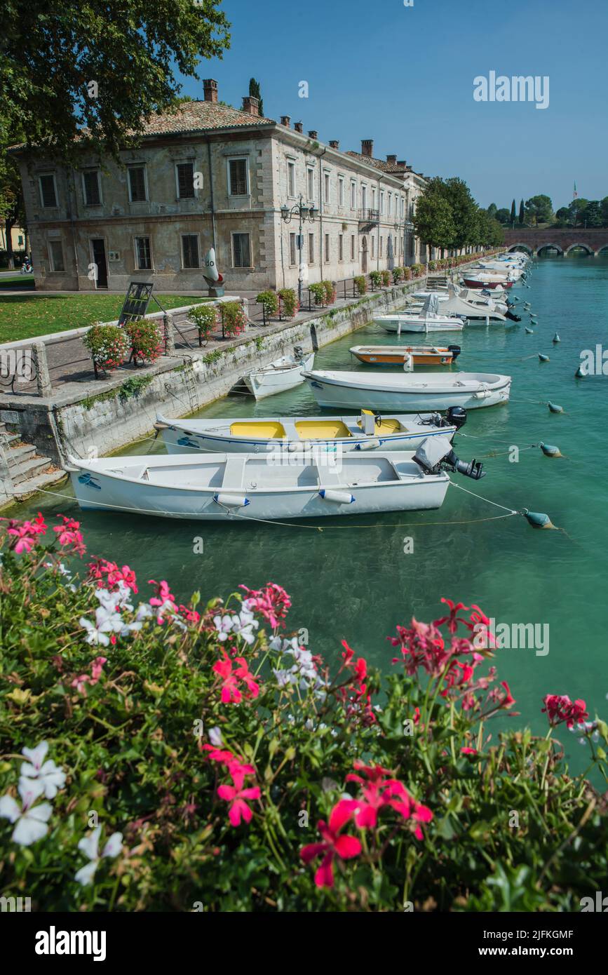 Small boats moored in Peschiera , Lake Garda, Italy.  Geraniums in the foreground Stock Photo