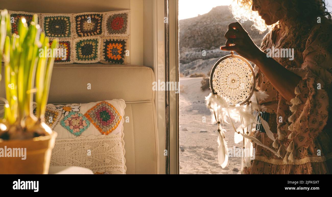 Boho woman traveler standing on the door of her alternative home camper van holding a dreamcatcer. Daydreaming lifestyle concept with free female Stock Photo