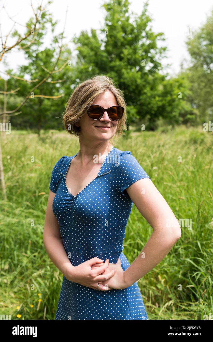 Portrait of an attractive thirty year old girl with a blue dress and sunglasses sitting at the Flemish countryside, Belgium. Stock Photo
