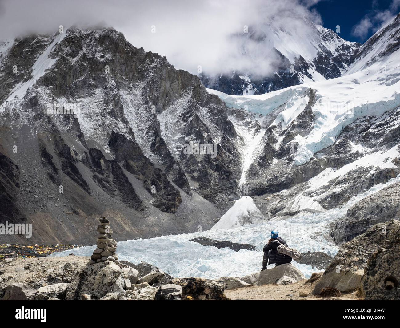 A traveller resting above the Khumbu Icefall. The fluted ridges of Khumbutse (6636m) tower above the yellow tents of Everest Base Camp. Stock Photo