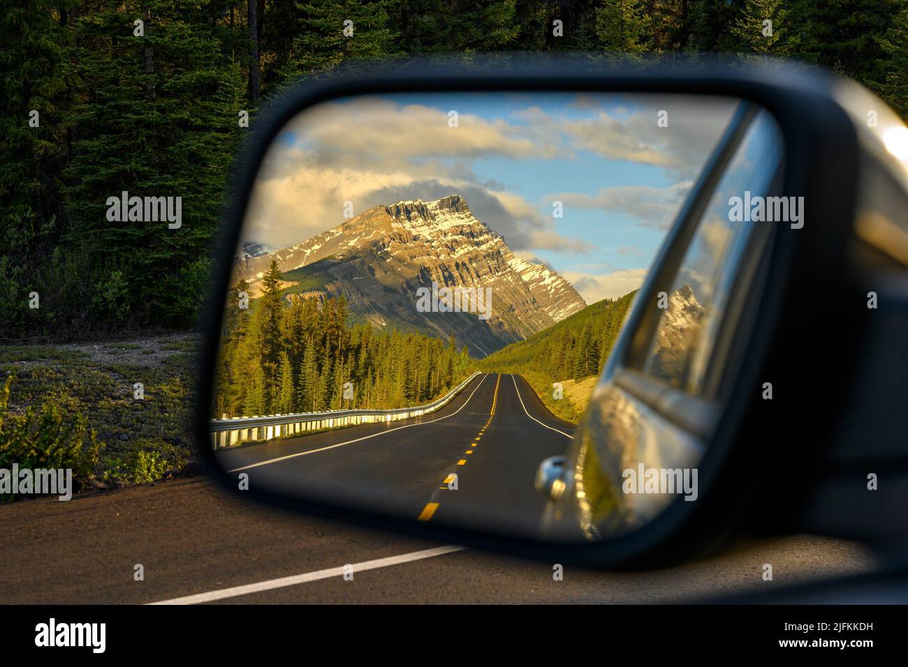 Driving a car through a mountain road that leads through the Canadian Rockies and watching the beautiful scenery in the rearview mirror in the Stock Photo