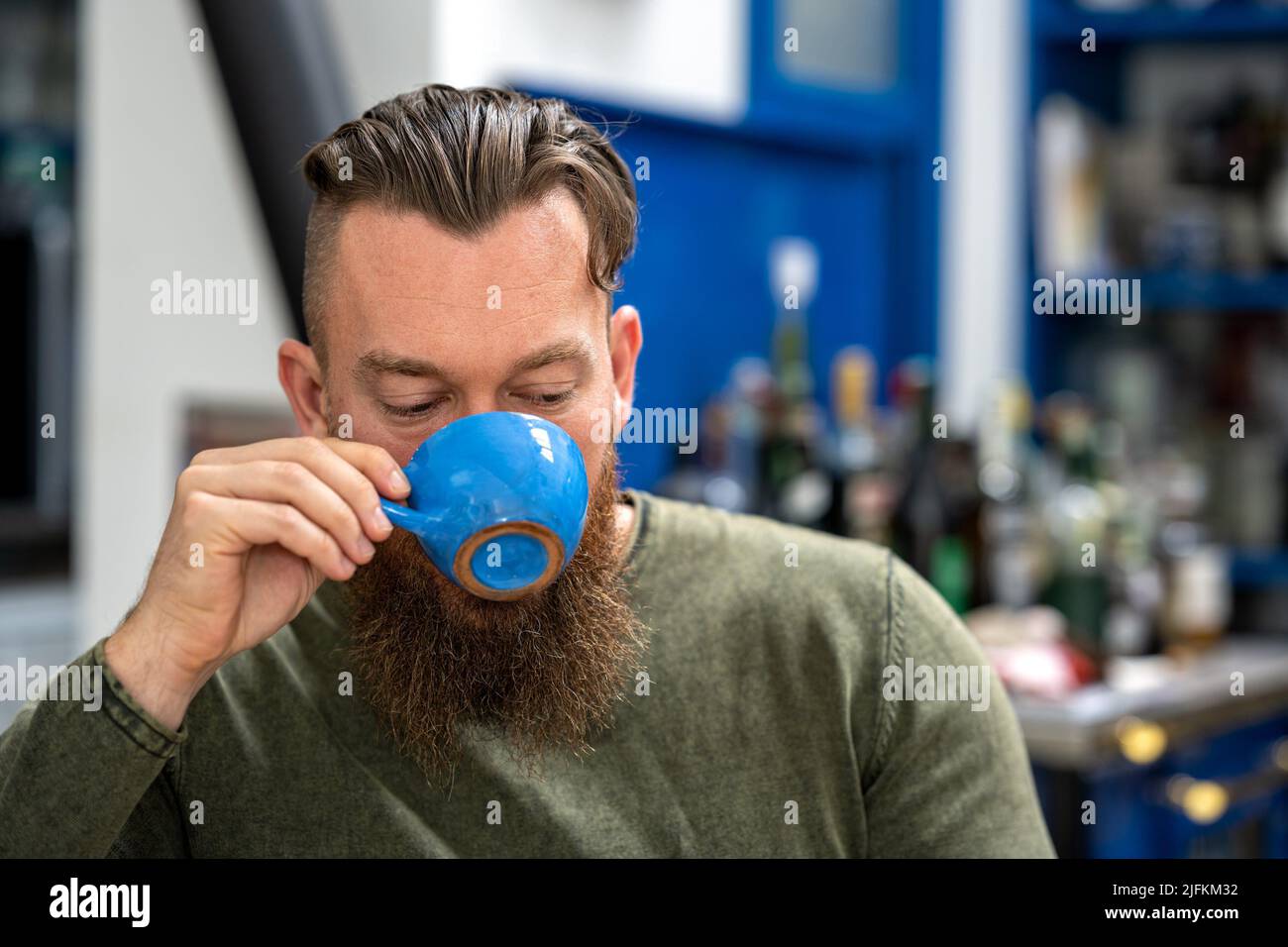 Dark tonal close up portrait of a young stylish handsome bearded Canadian man enjoying coffee in a country bar. Stock Photo