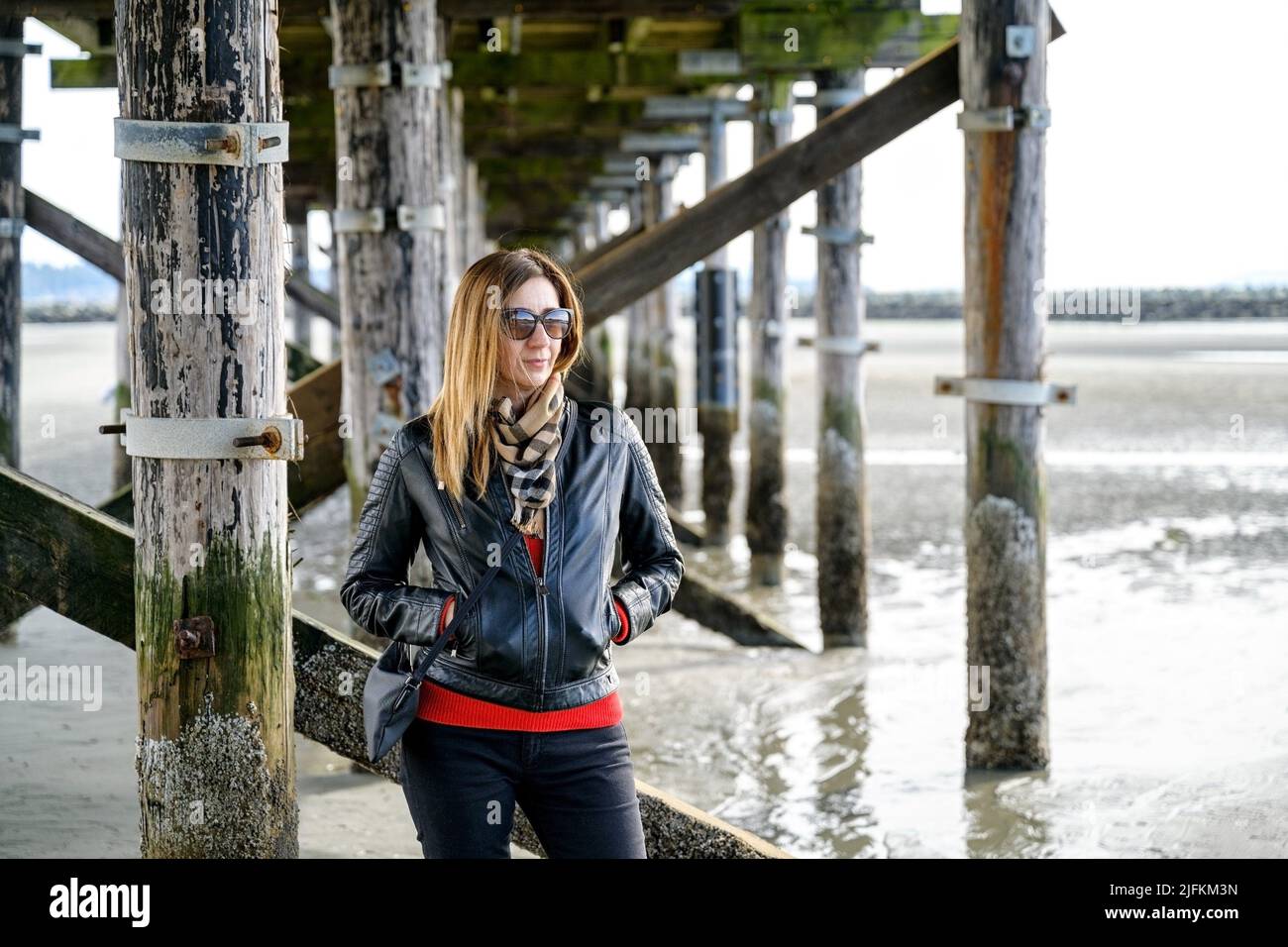 Stylish, well-dressed casual middle-aged woman looking sideway and standing underneath Canada's longest pier, the 470-metre-long White Rock Pier in Stock Photo