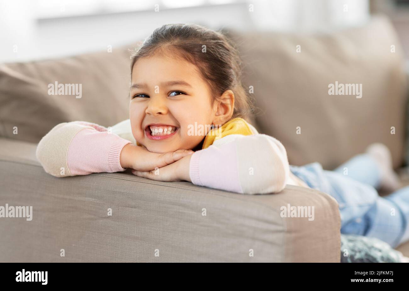 happy smiling little girl lying on sofa at home Stock Photo - Alamy