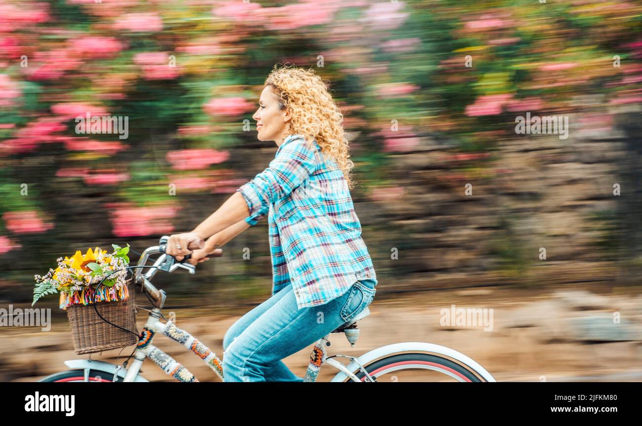 Happy adult woman ride a bike outdoor with flowers in background. Environment and green transport with bycicle. Cheerful modern female people enjoy Stock Photo