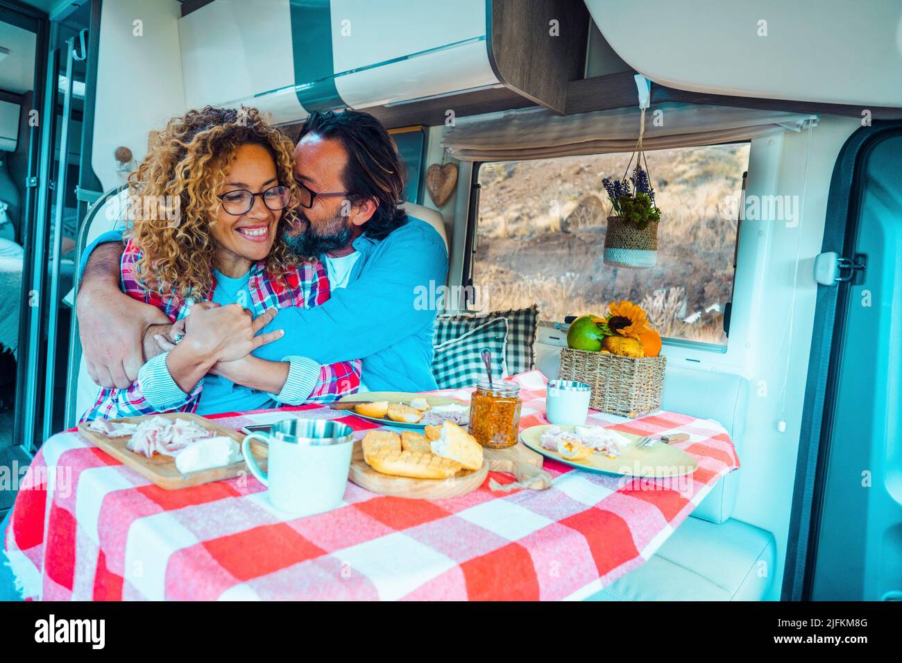 Cheerful couple hugging inside a camper van during lunch time. Concept of travel and holiday vacation. Renting of rv vehicle for adult people. On the Stock Photo