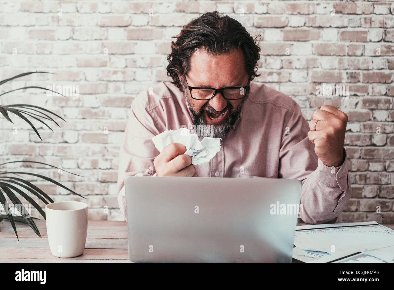 Angry man in bad expression looking a computer display with bad notifications. Adult people working on line with stress and desperation emotions. Stock Photo
