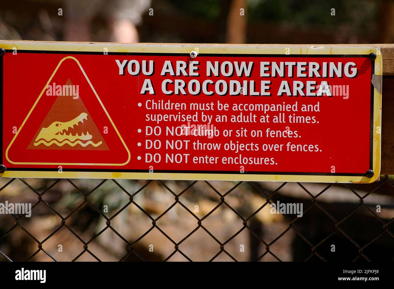 Red warning sign on fence in wildlife park telling people to keep away from crocodiles and not to enter their enclosure. Queensland, Australia. Stock Photo
