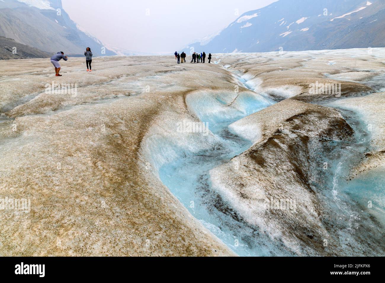 Surface melt water flowing through sinuous channel on the Athabasca Glacier. There are some people in the background exploring the glacier by walking Stock Photo