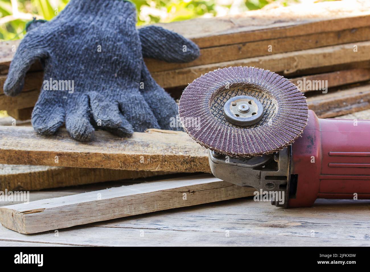 Electric sandpaper tool on wooden table with a pile of wood behind