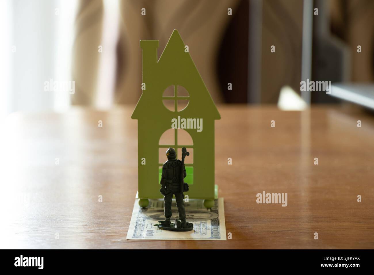 Children's plastic soldier stand on dollars, take a small green house on the table to the apartment, buying a house for a military soldier, success an Stock Photo