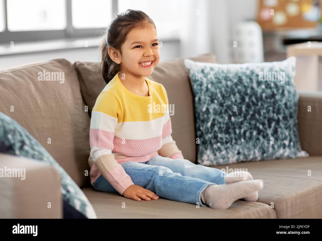 happy smiling little girl sitting on sofa at home Stock Photo - Alamy