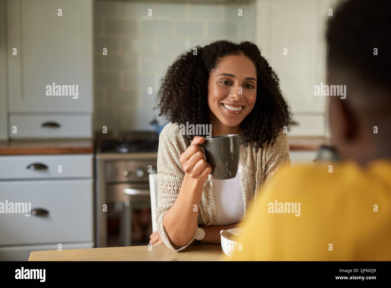 Smiling young African woman drinking coffee and talking with her husband over breakfast at a kitchen table in the morning Stock Photo