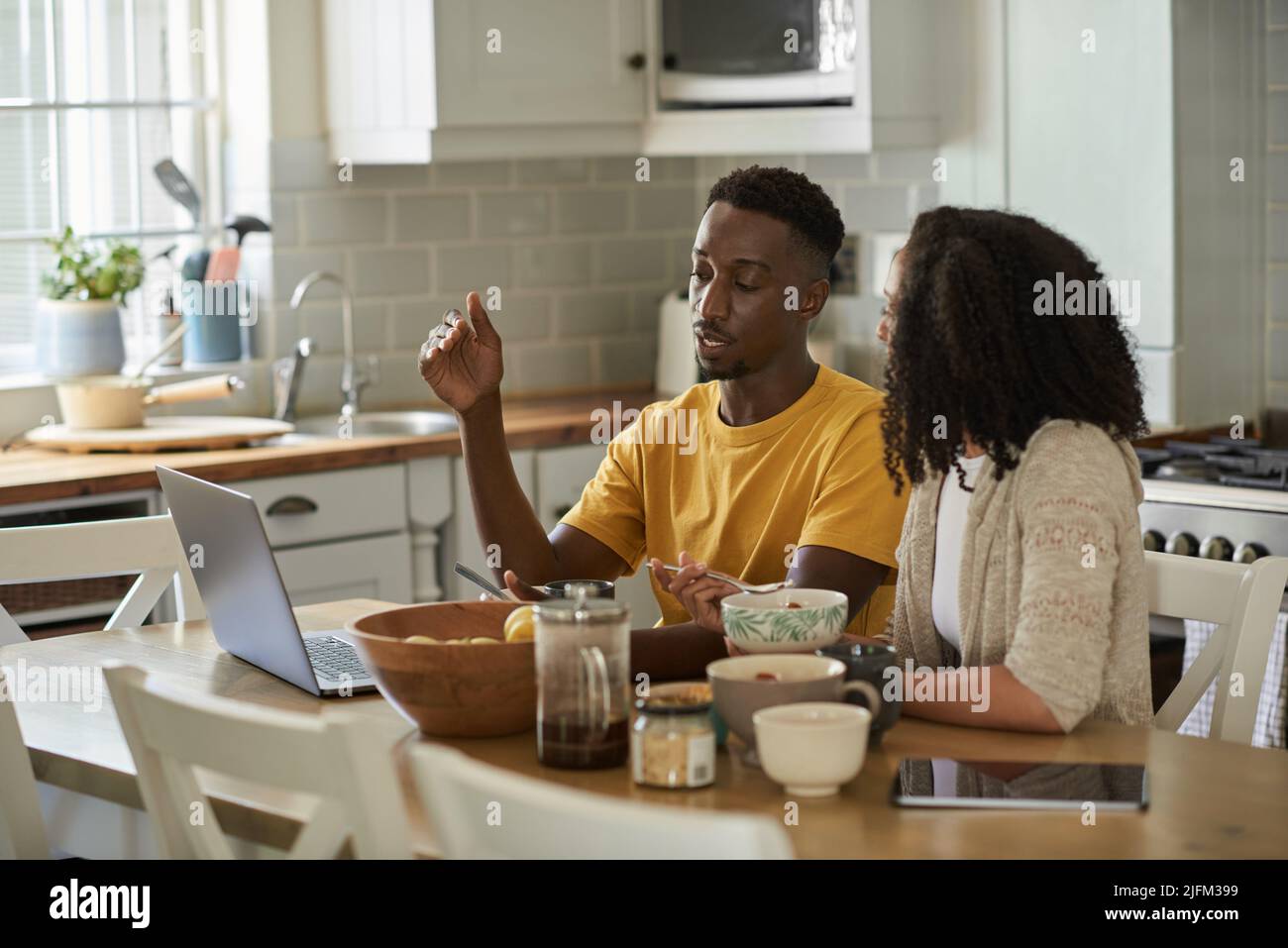Young multiethnic couple talking and using a laptop at breakfast Stock Photo