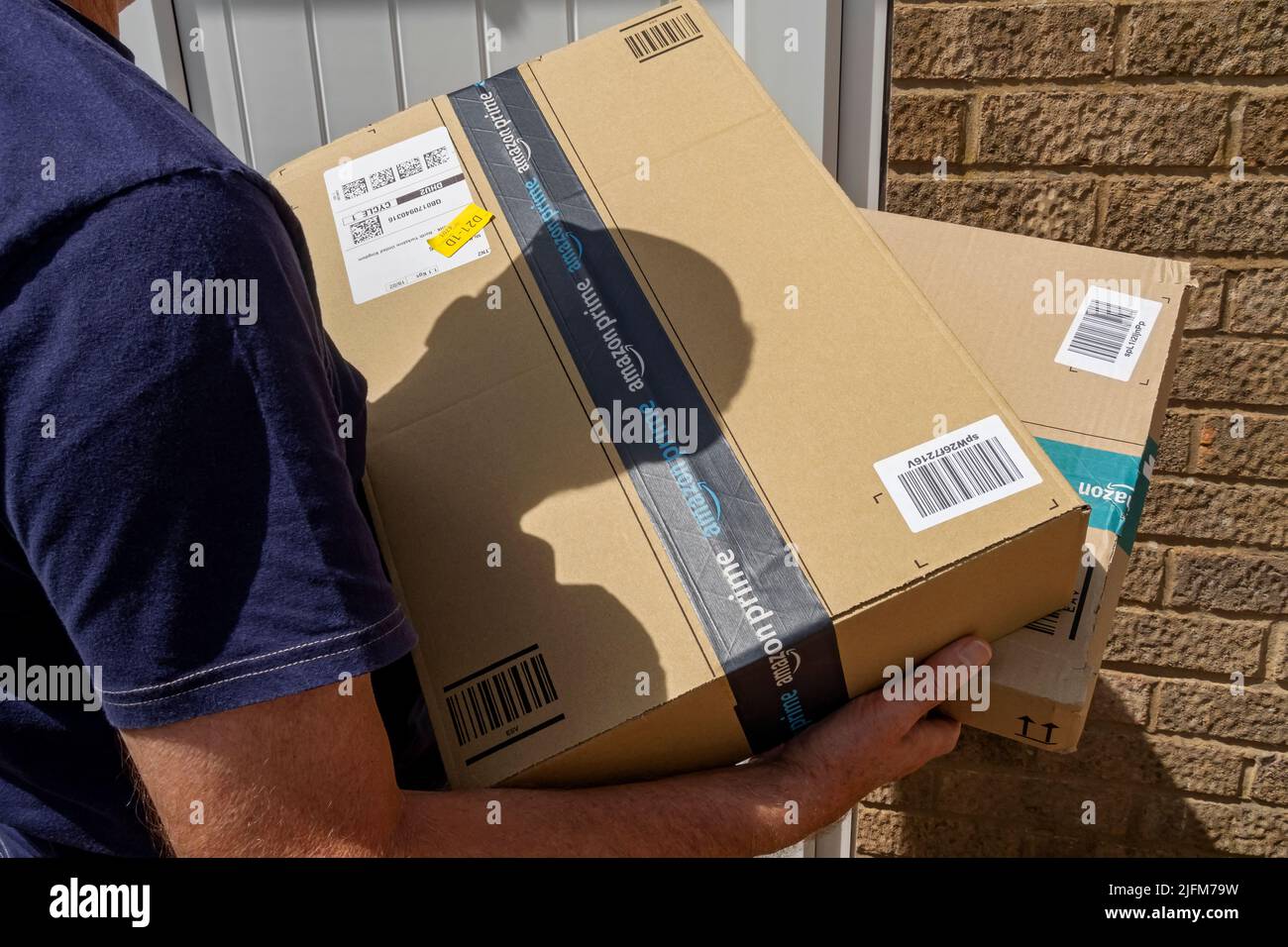 Delivery driver man person holding carrying delivering online shopping Amazon prime box boxes delivery parcels parcel England UK Britain Stock Photo