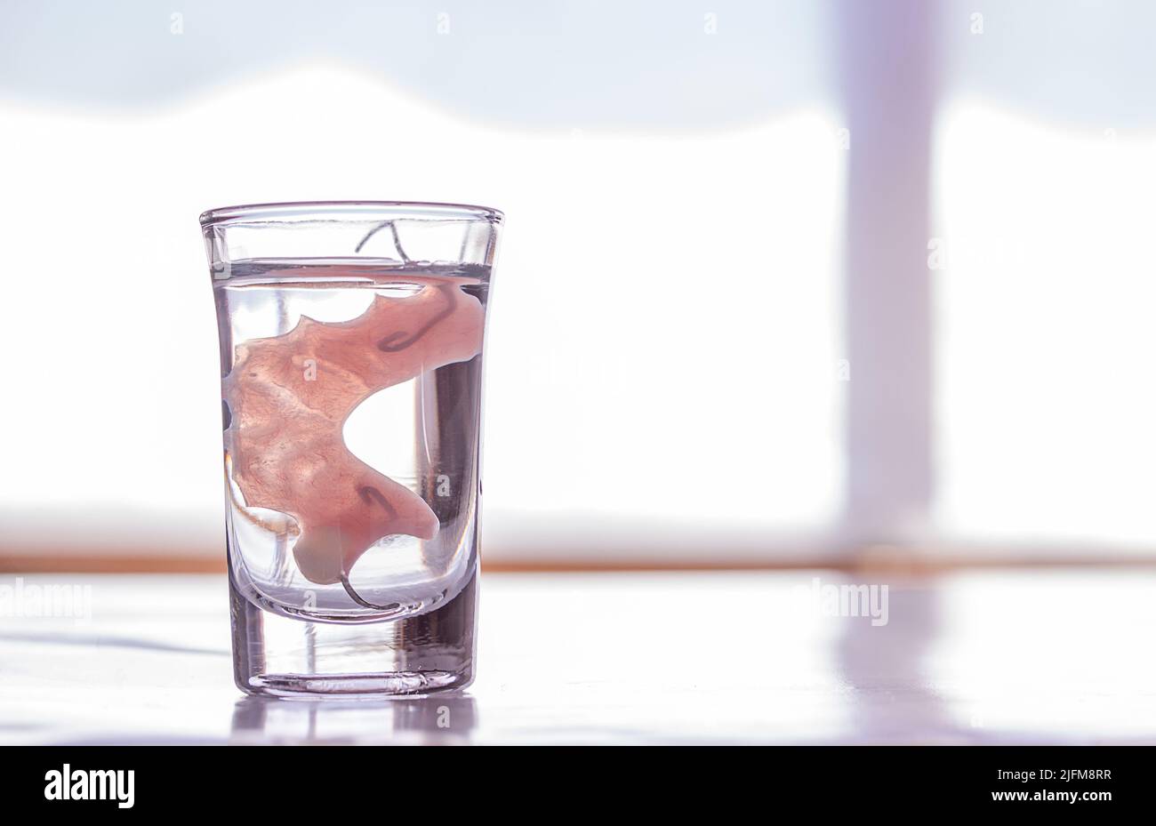 Close up acrylic dentures immersed in a glass of water,table in the