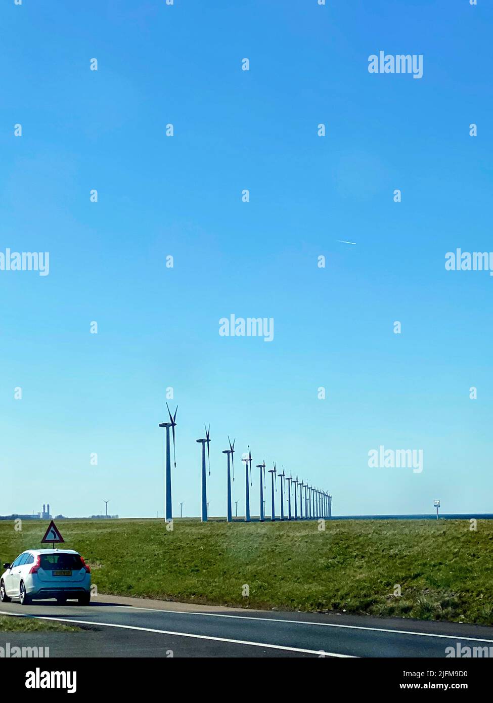 Wind turbines on a dyke near a road with a car, Netherlands Stock Photo