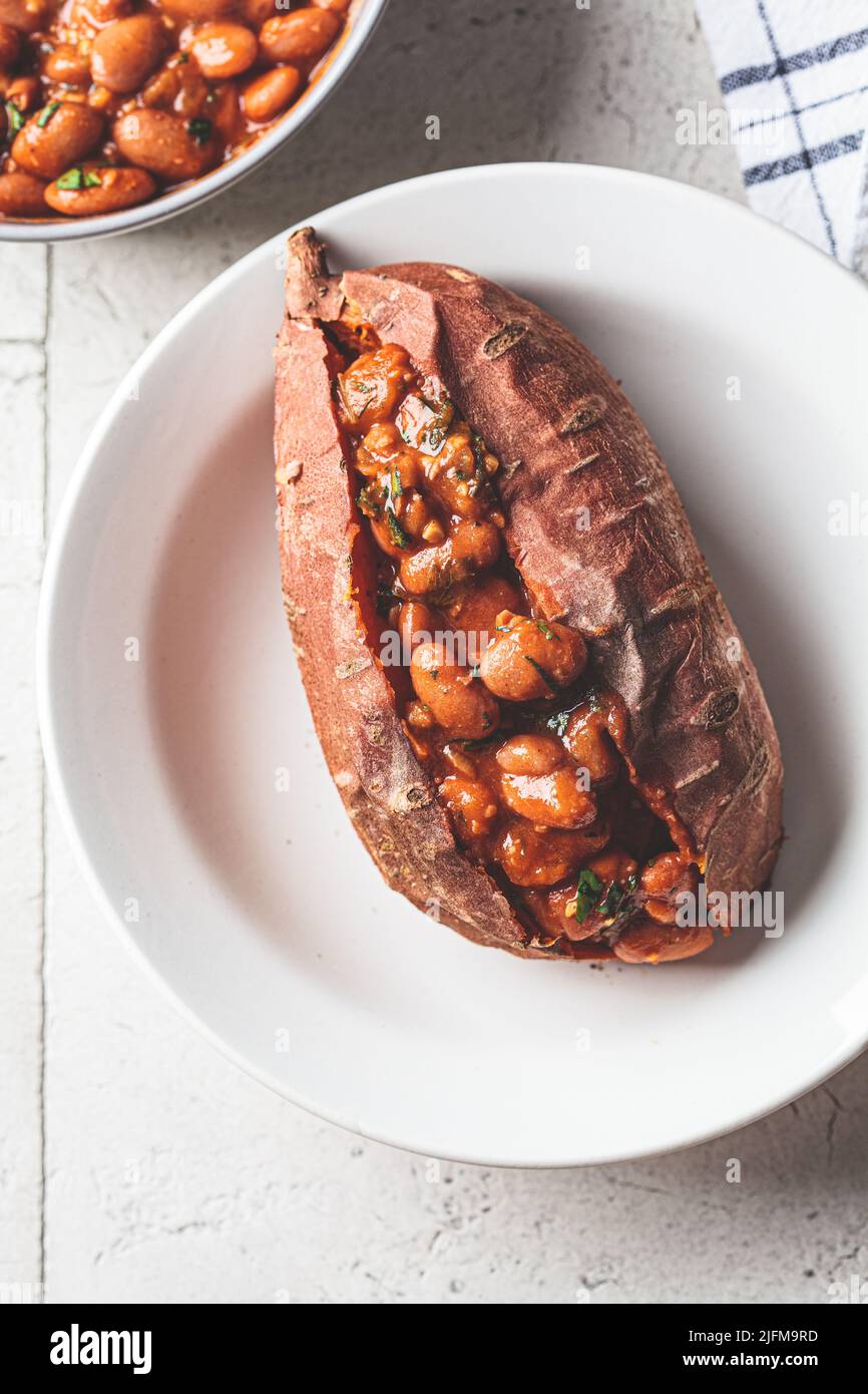 Baked sweet potato stuffed with beans in tomato sauce, top view. Vegan