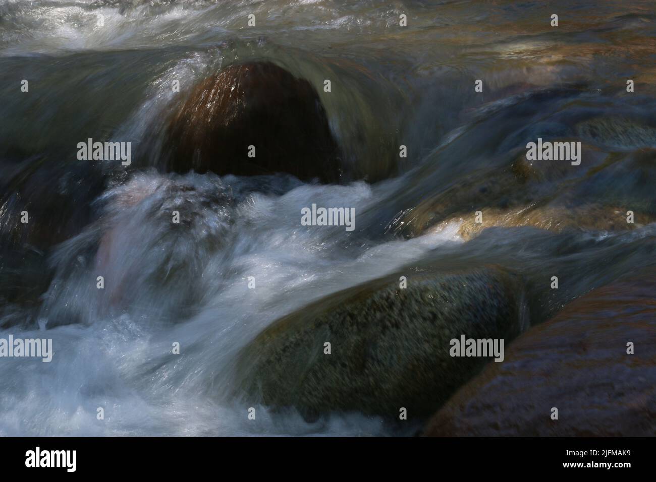 Ein schnell fließender Gebirgsbach umströmt einen Felsen im Flussbett Stock Photo