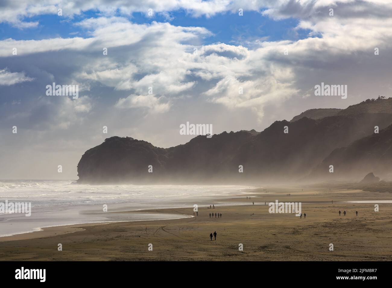 The black sand beach at Piha, New Zealand, looking towards Te Waha Point. A strong wind is blowing spray off the ocean Stock Photo
