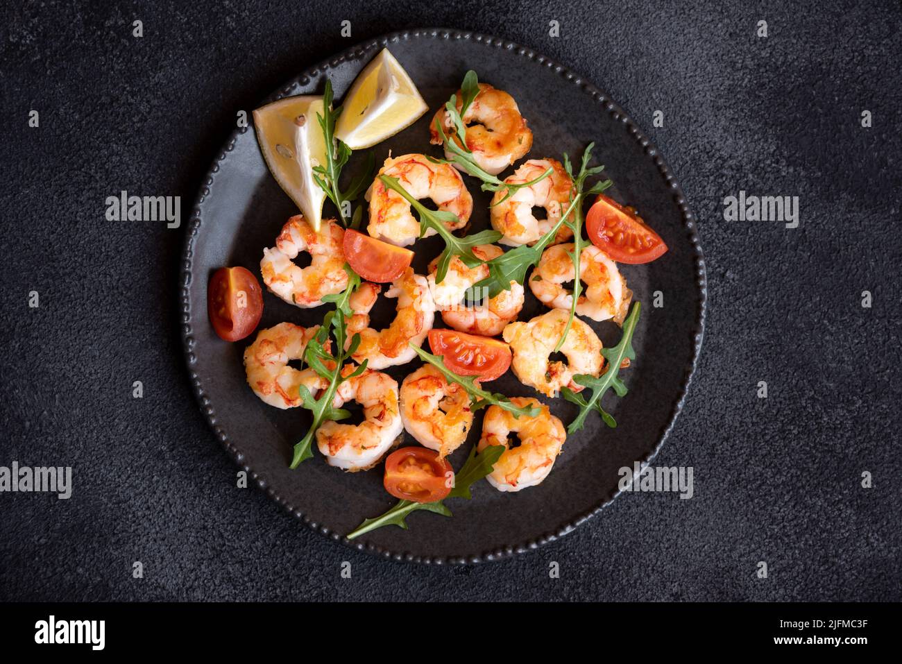 Roasted shrimps with tomatoes and arugola on black plate Stock Photo