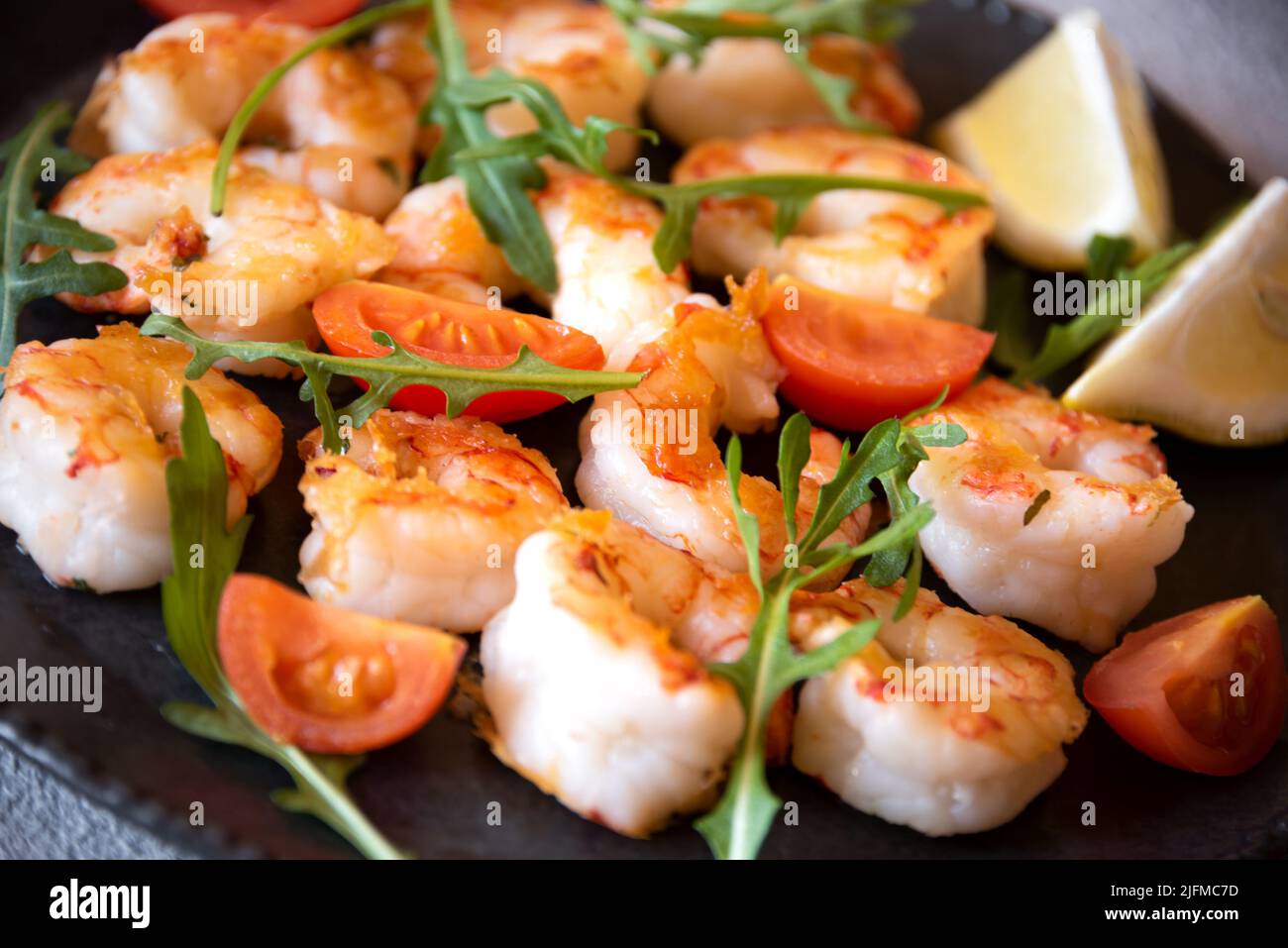 Roasted shrimps with tomatoes and arugola on black plate Stock Photo