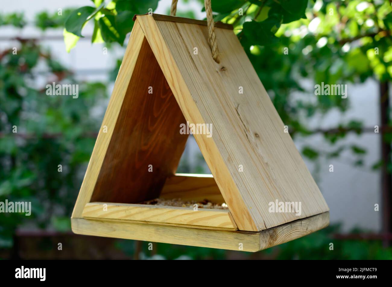 Small wooden birdhouse is hanging on a natural rope on the tree. Waiting for the birds. DIY birdhouse. Background picture. Stock Photo