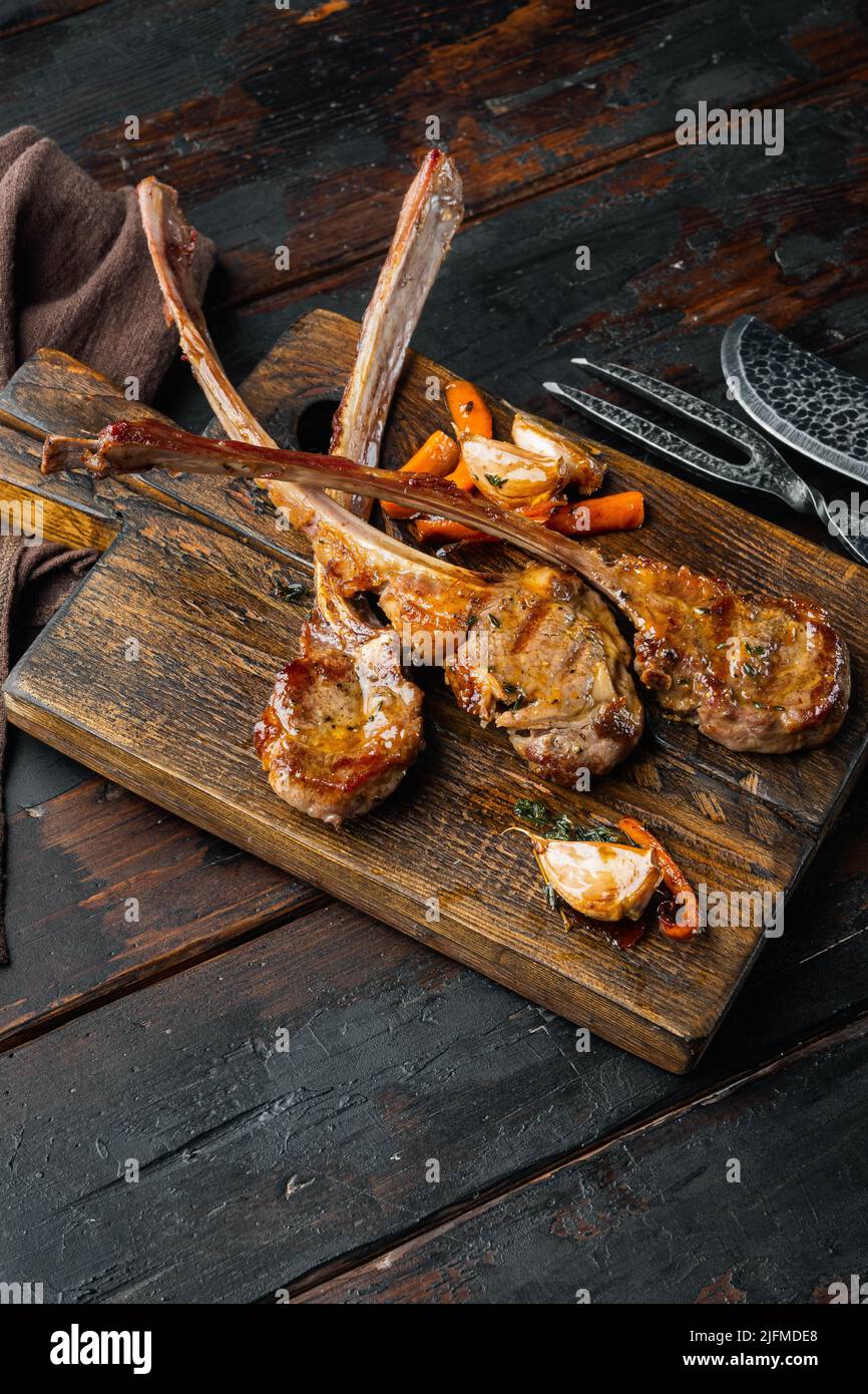 Homemade Cooked Lamb Chops with garlic and Carrots set, on wooden serving board, on old dark wooden table background , with copyspace and space for te Stock Photo