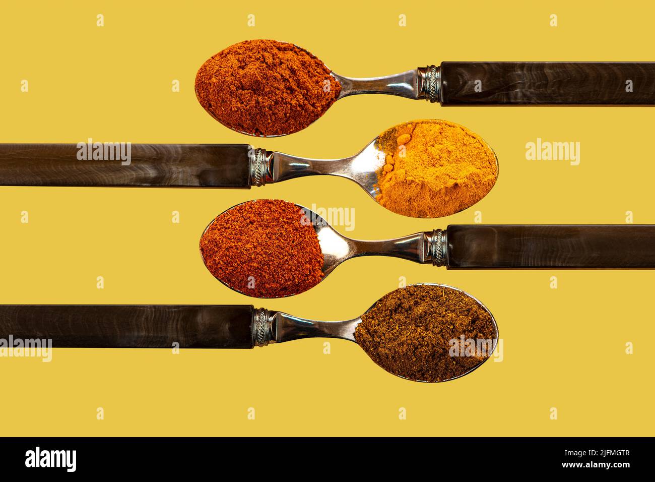 A selection of cayenne pepper turmeric chili curry powder spices used in Indian cooking on a colourful yellow background Stock Photo