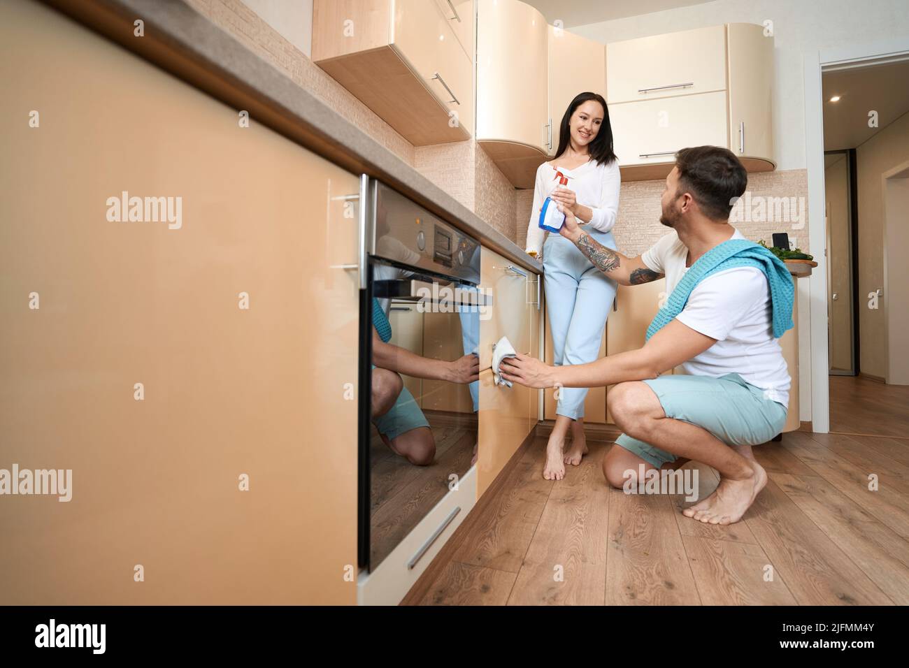 Husband passing detergent to wife while cleaning cupboard drawers Stock Photo