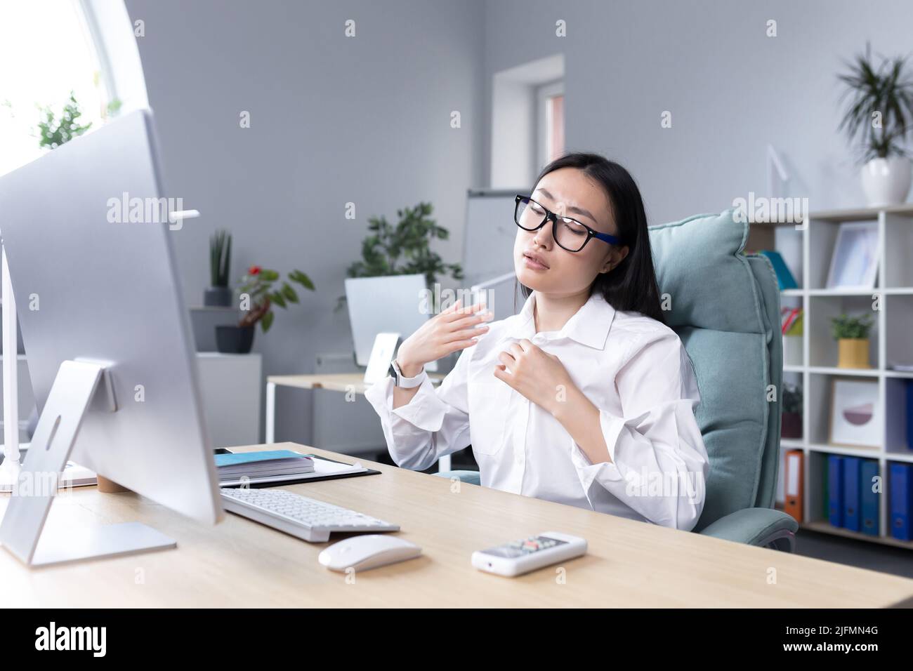 Heat in the office, Asian woman trying to freshen up, business woman working at the computer, waving her hands to cool down. Stock Photo