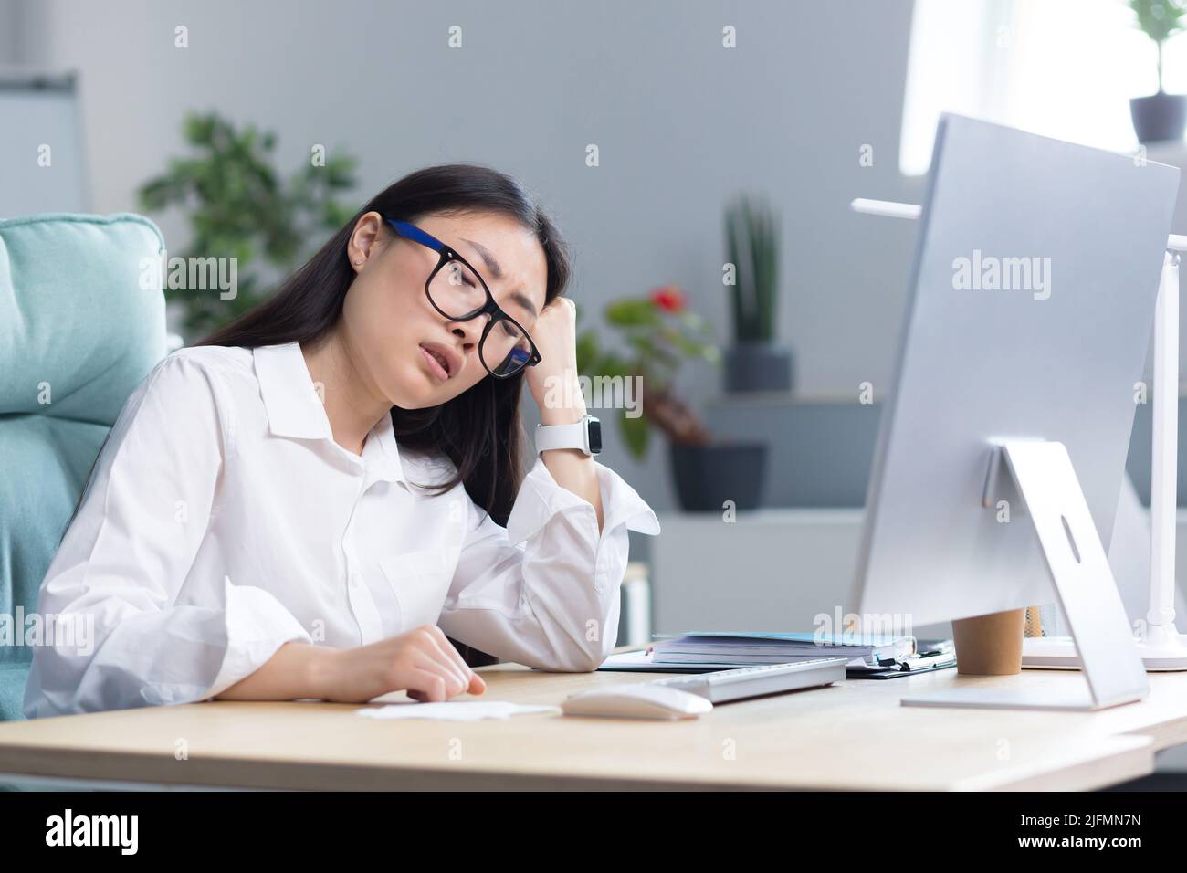A sad Asian business woman despairs of her abilities, is depressed and works in the office at the computer. Stock Photo