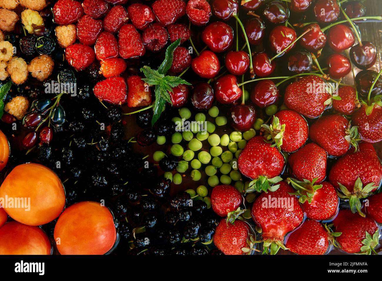 Assorted fresh seasonal fruits and berries: strawberries, apricots, cherries, mulberry, raspberries washing under natural light. Healthy, natural dessert, organic food. Stock Photo