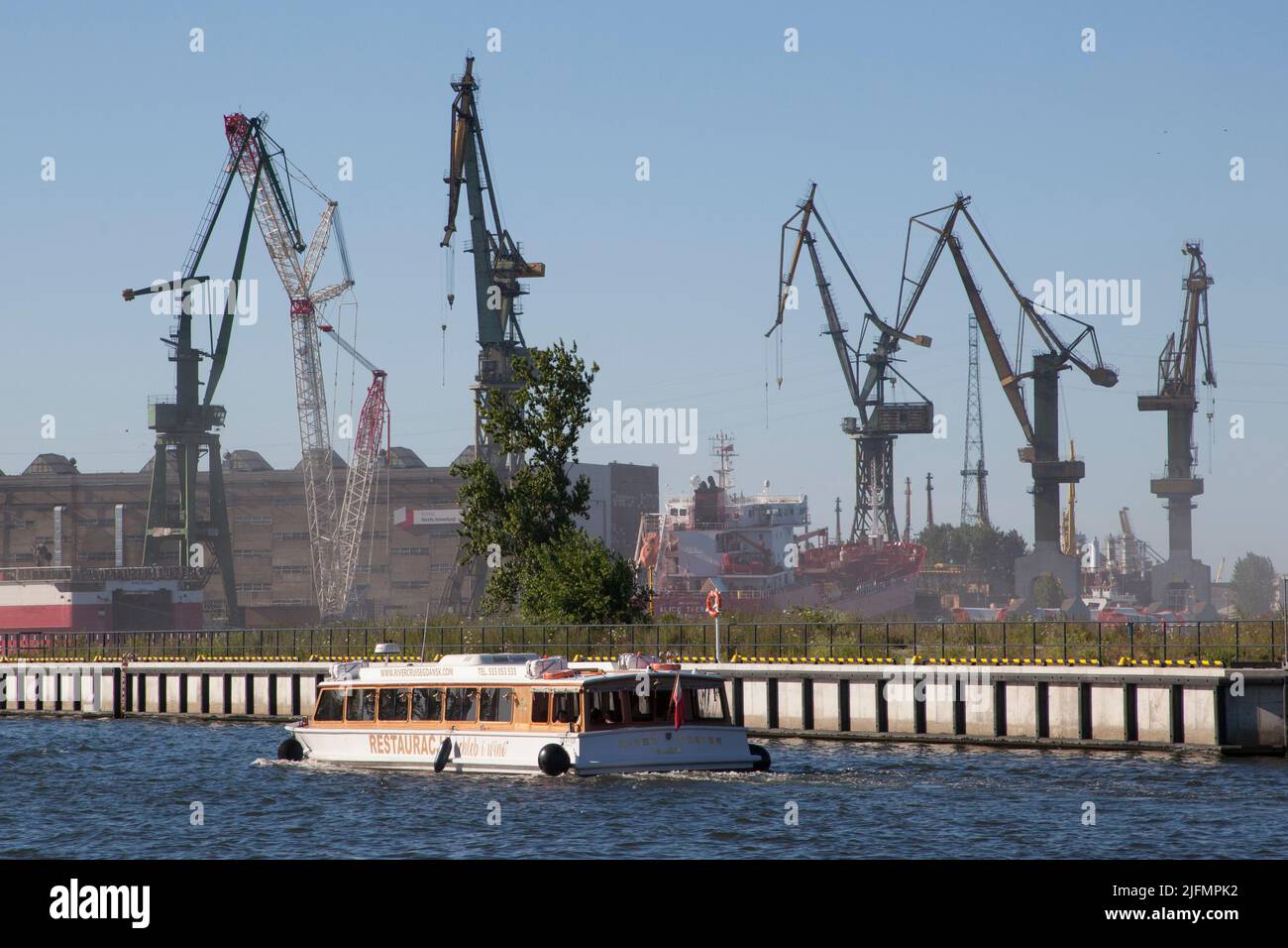 River cruise by Chleb i Wino restaurant boat passes in front of cranes in Gdansk Shipyard, Poland -  River cruise by Chleb i Wino Stocznia Gdansk, Pol Stock Photo
