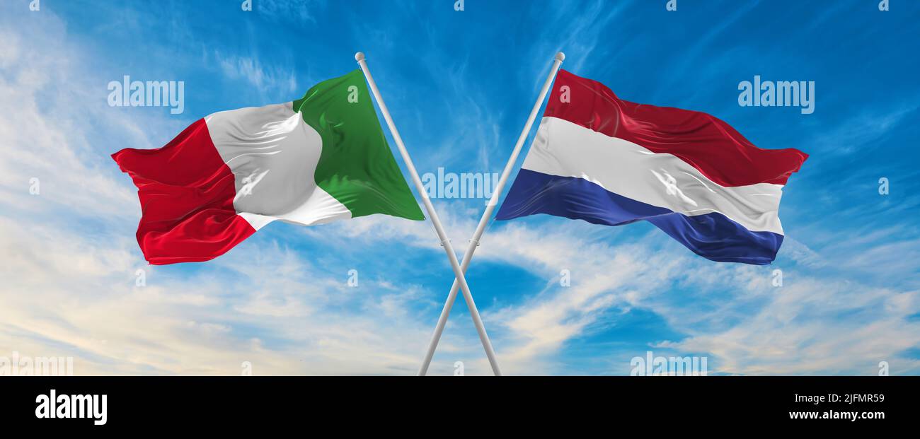 two crossed flags Italy and Netherland waving in wind at cloudy sky ...