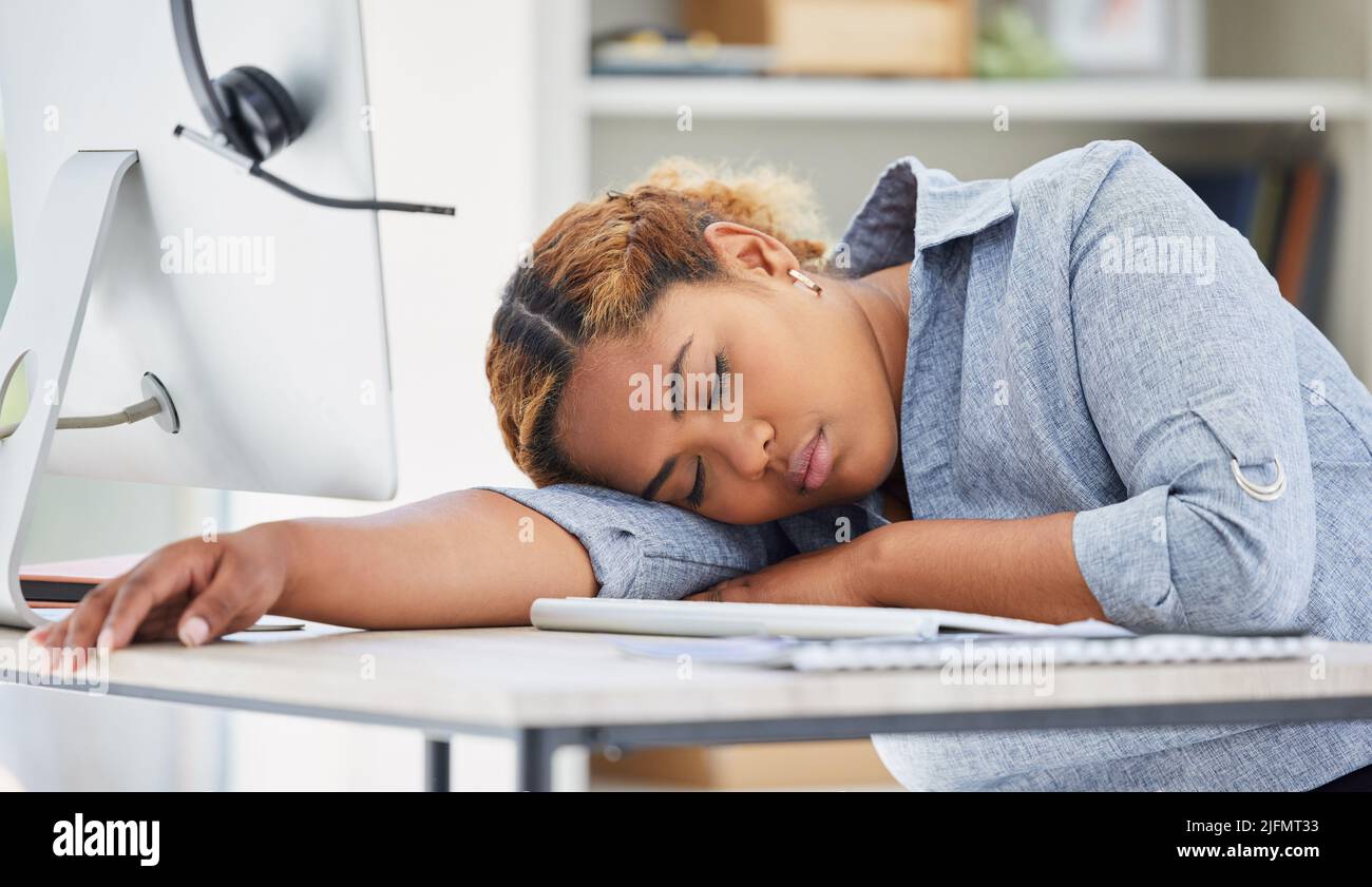 One exhausted african american call centre agent sleeping in an office. Businesswoman feeling overworked, tired and demotivated while operating Stock Photo