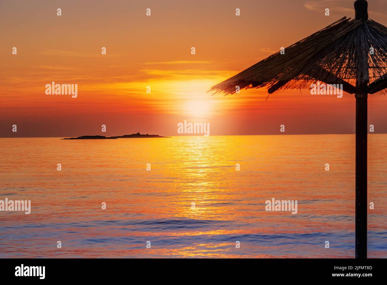 Beautiful sunset by the sea with the silhouette of a parasol and a island in background, to relax on vacation Stock Photo