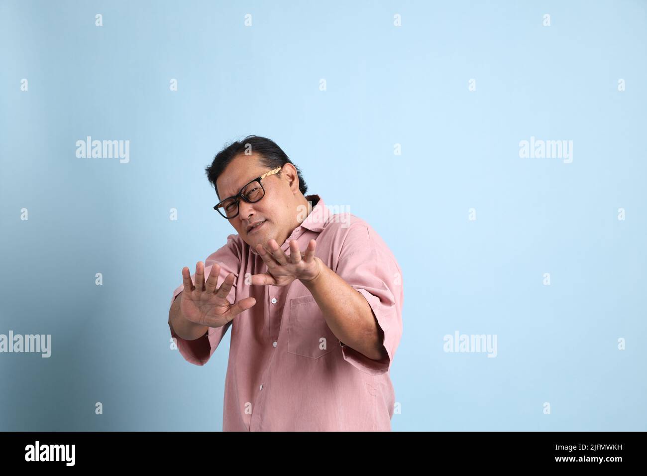 The adult Asian man with pink shirt standing on the blue background. Stock Photo