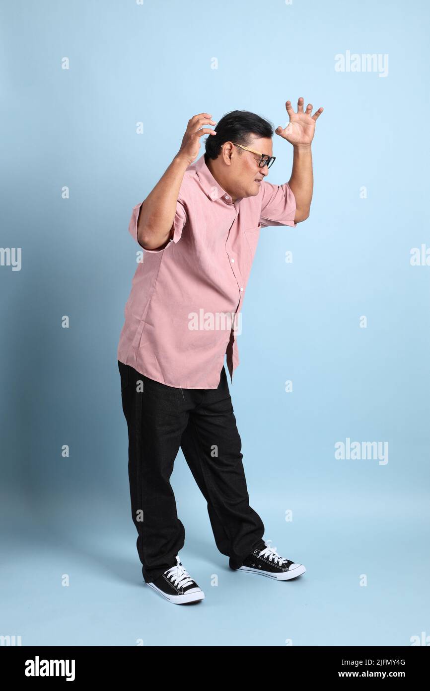 The adult Asian man with pink shirt standing on the blue background. Stock Photo