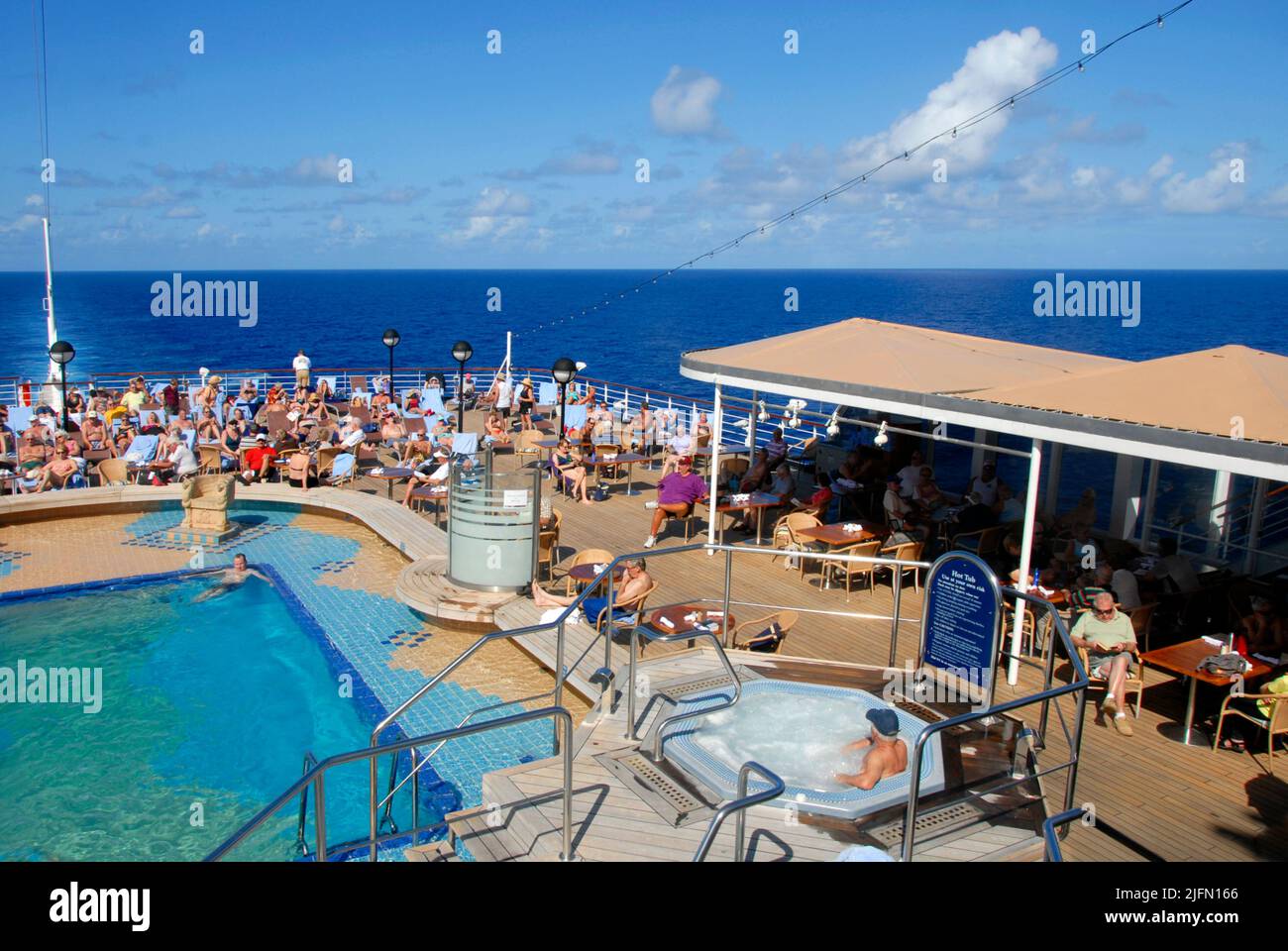 Passengers relaxing round the swimming pool at the rear of a cruise liner at sea in the Caribbean Stock Photo