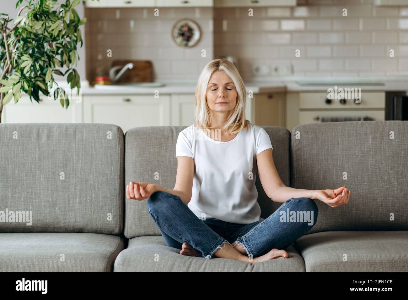 Calm satisfied peaceful middle aged female sits on sofa at home and ...