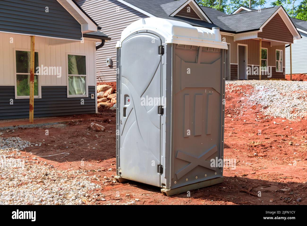 A portable restroom is being used at a construction site near a house that is being built Stock Photo